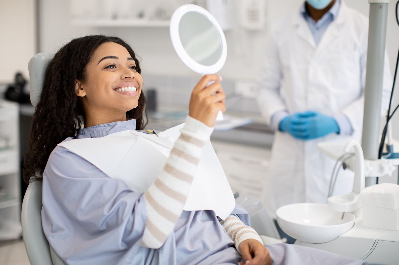 A smiling patient checking her teeth in a hand mirror during a dental visit