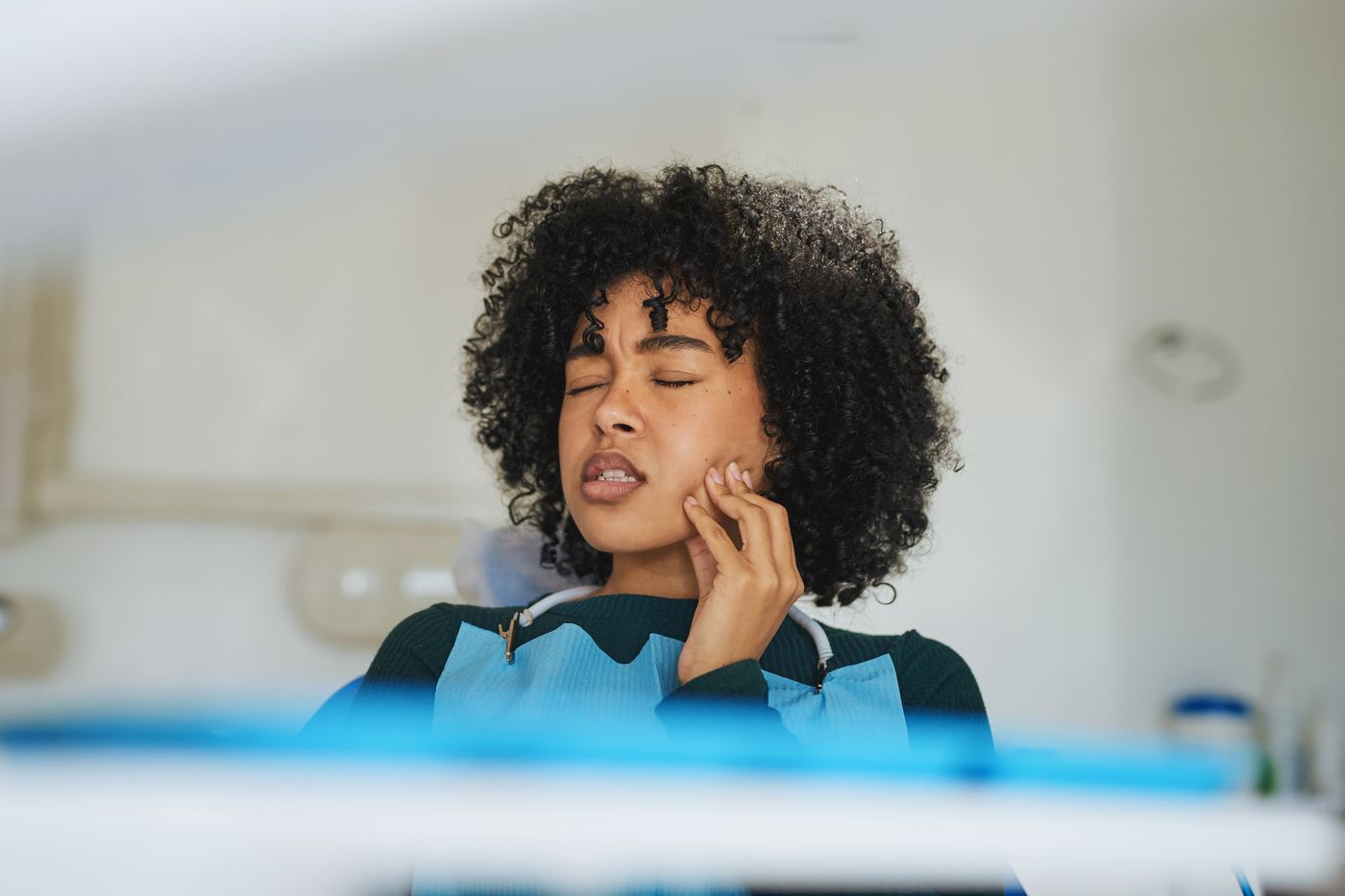 Woman with curly hair touching her jaw in a dental office setting showing discomfort