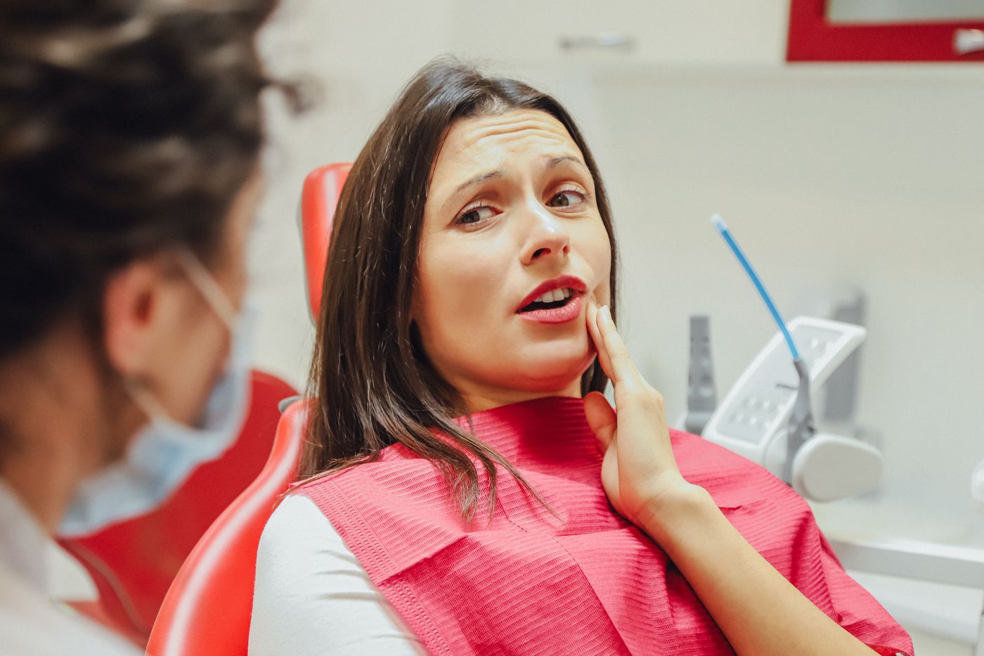 Woman wincing in pain while talking to her dentist in Santa Barbara CA