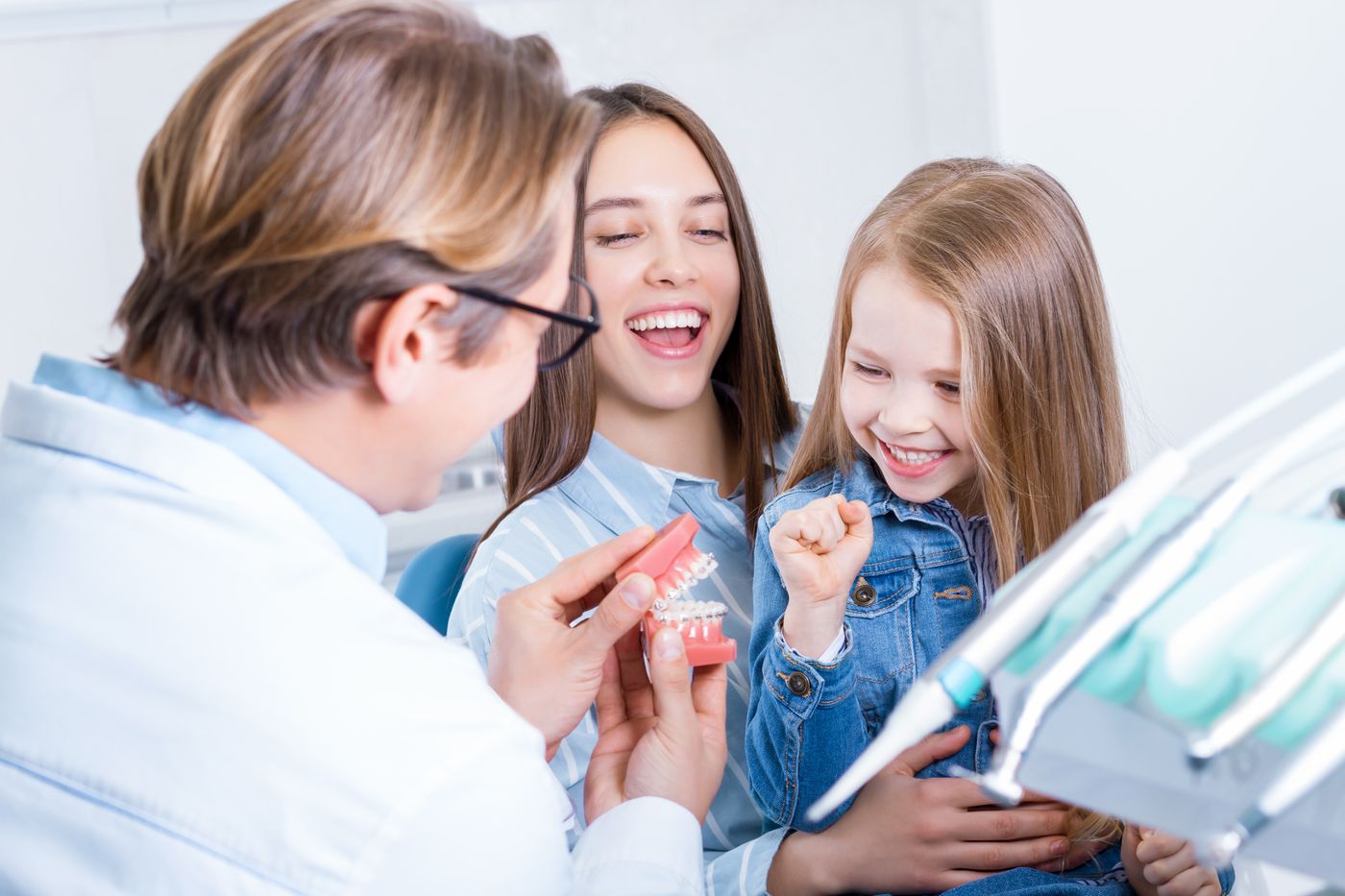 A dentist showing a tooth model to a smiling mother and daughter