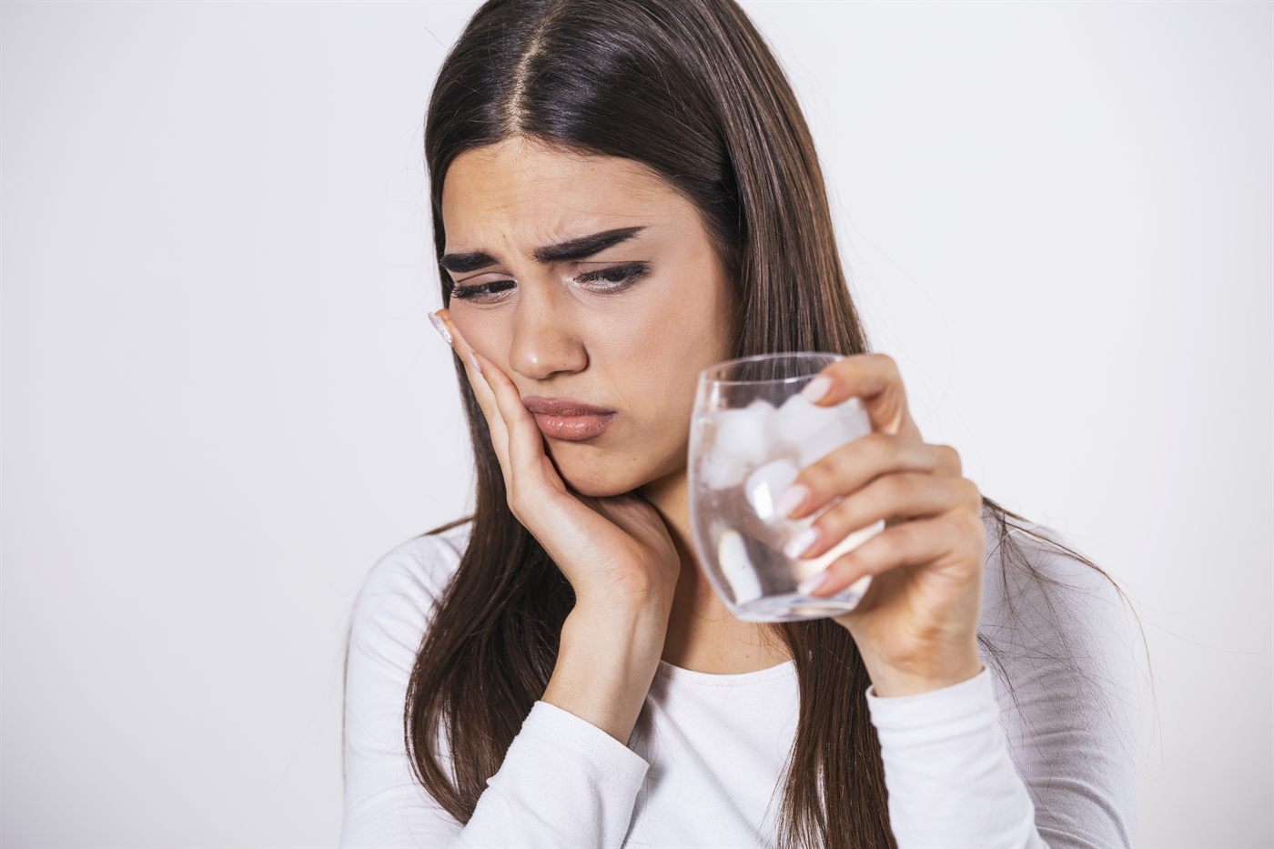 Woman wincing from tooth sensitivity while holding a glass of ice water in Santa Barbara CA